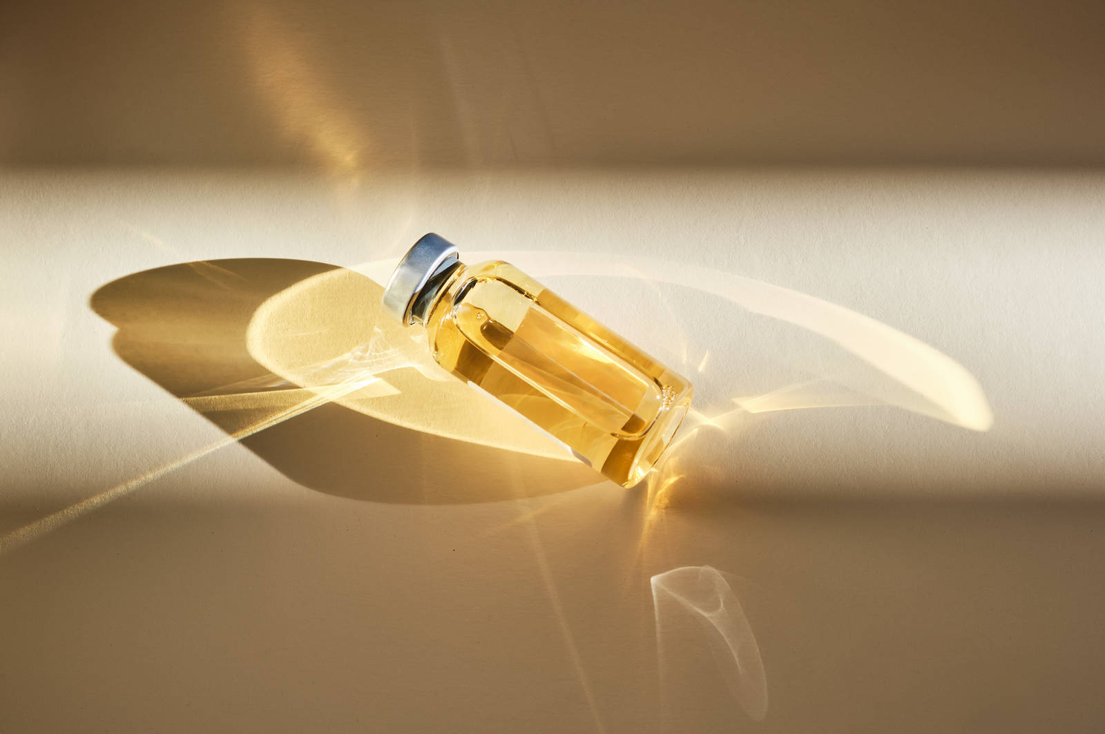 Elegant glass bottle filled with golden oil, casting soft shadows on a light background.